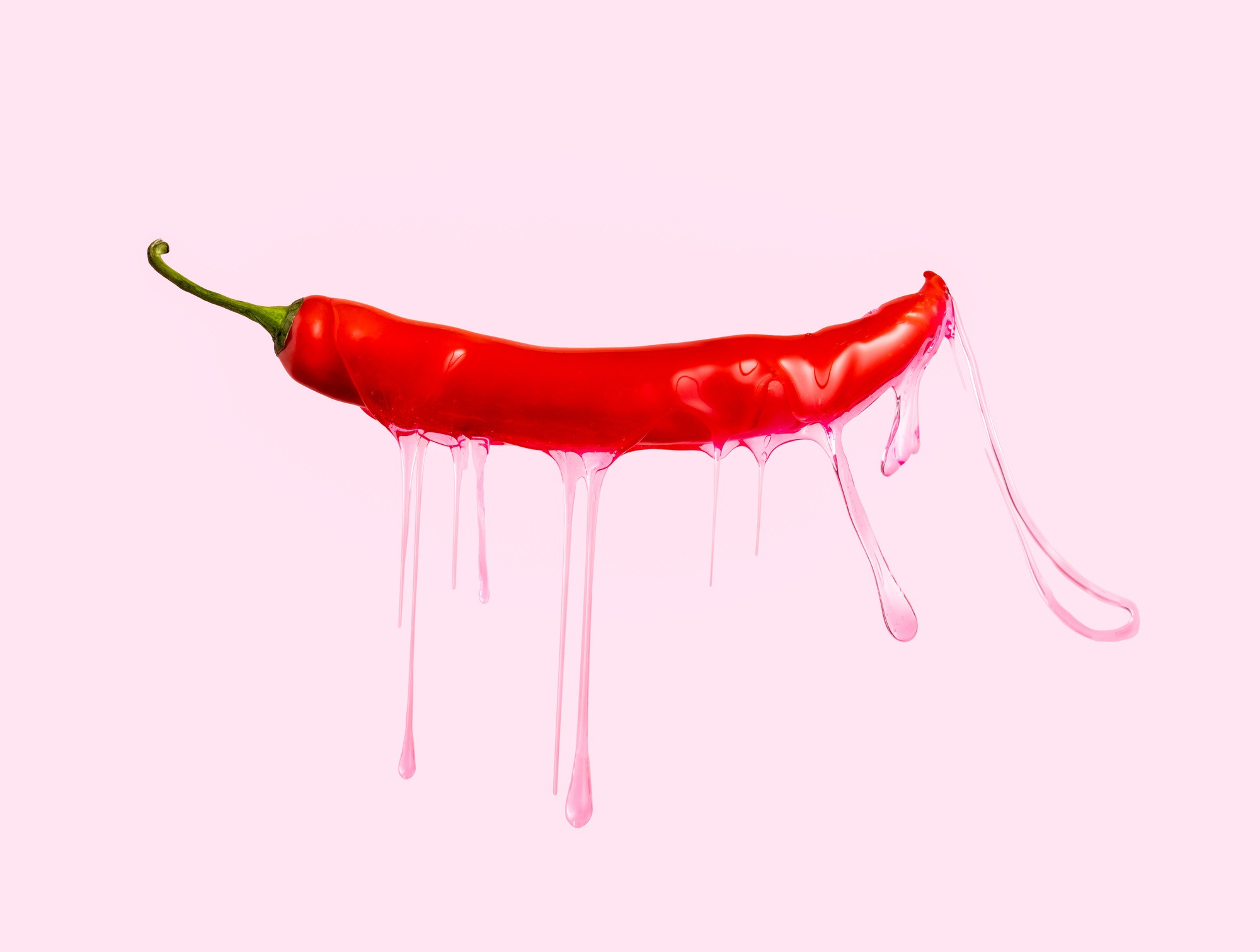 Peperoncino rosso con gel rosa gocciolante su sfondo rosa.
