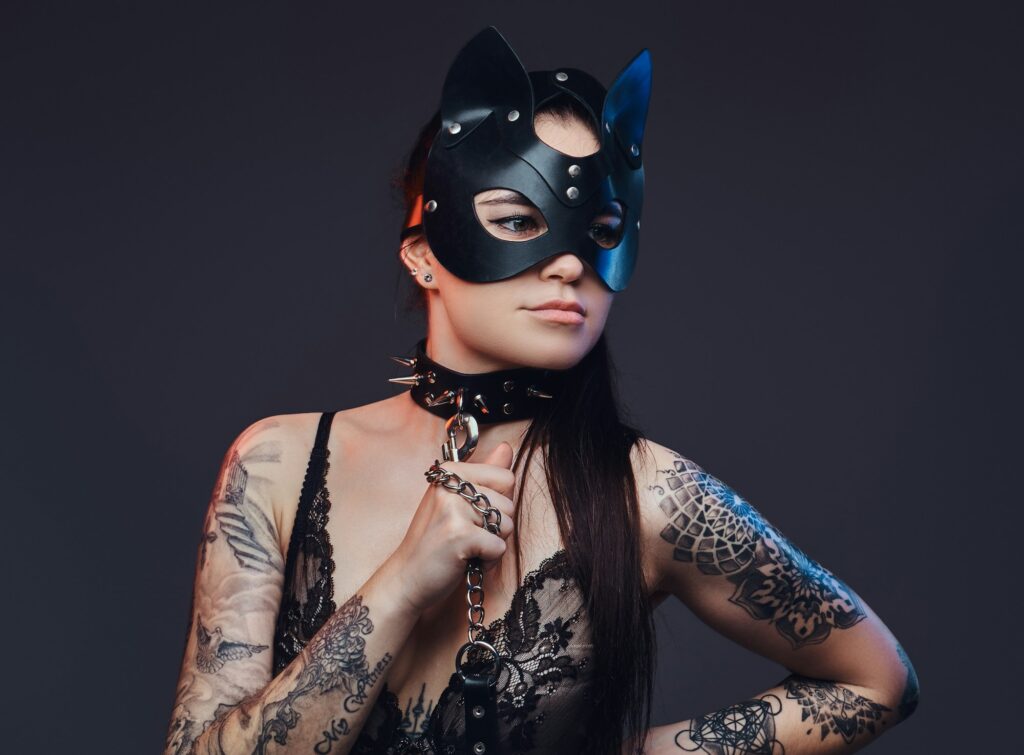 Sexy woman wearing black lingerie in BDSM cat leather mask and accessories posing on dark