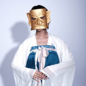 Ätherische Figur mit goldener Maske und elegantem Gewand, die Tradition und moderne Anziehungskraft miteinander verbindet.