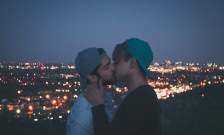 Una gioiosa coppia gay si bacia sotto le luci ipnotiche della città al crepuscolo, abbracciando il proprio amore in un vibrante contesto urbano.