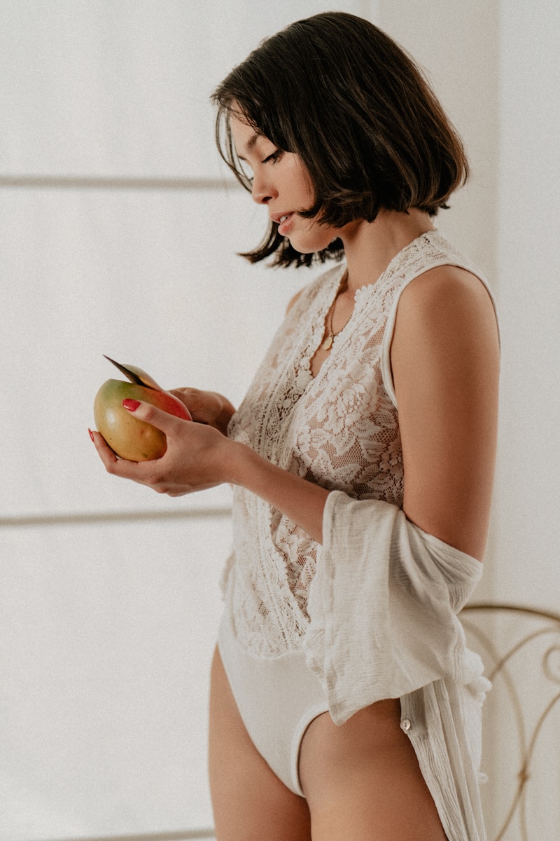 una mujer con un body blanco sosteniendo una manzana