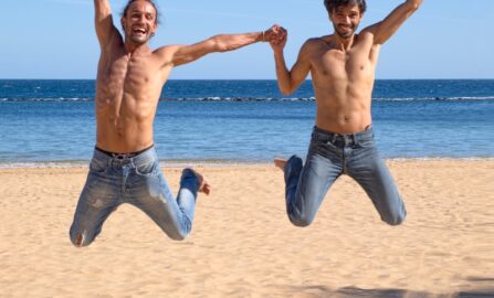 Glada vänner som hoppar på en vacker strand Två män hoppar över brun strandsand