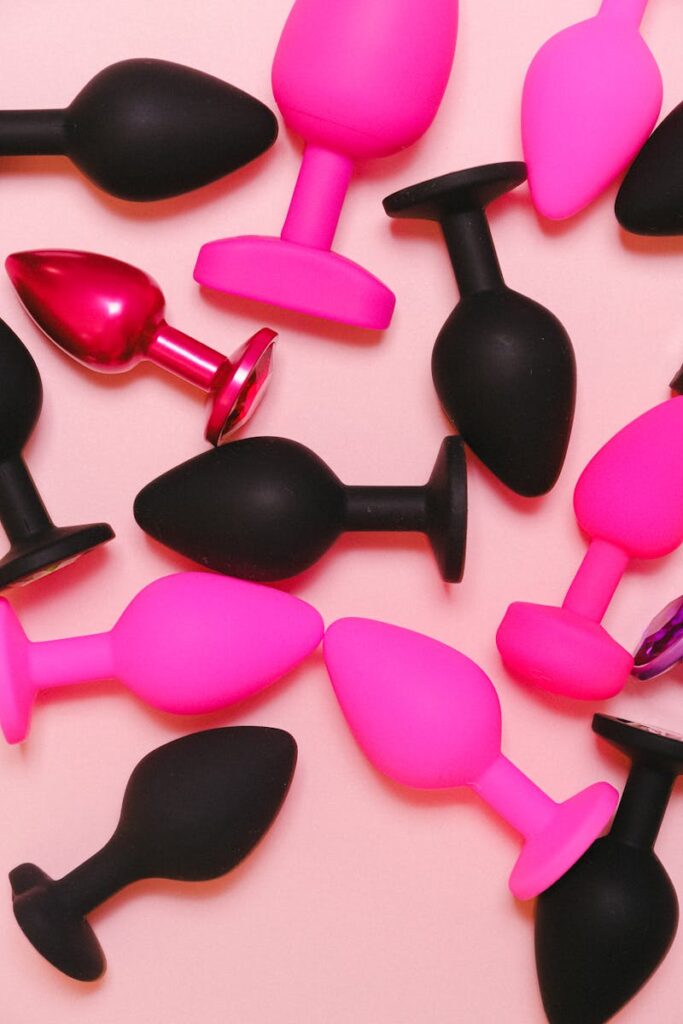 Bright and colorful collection of silicone adult toys on a pastel pink background.