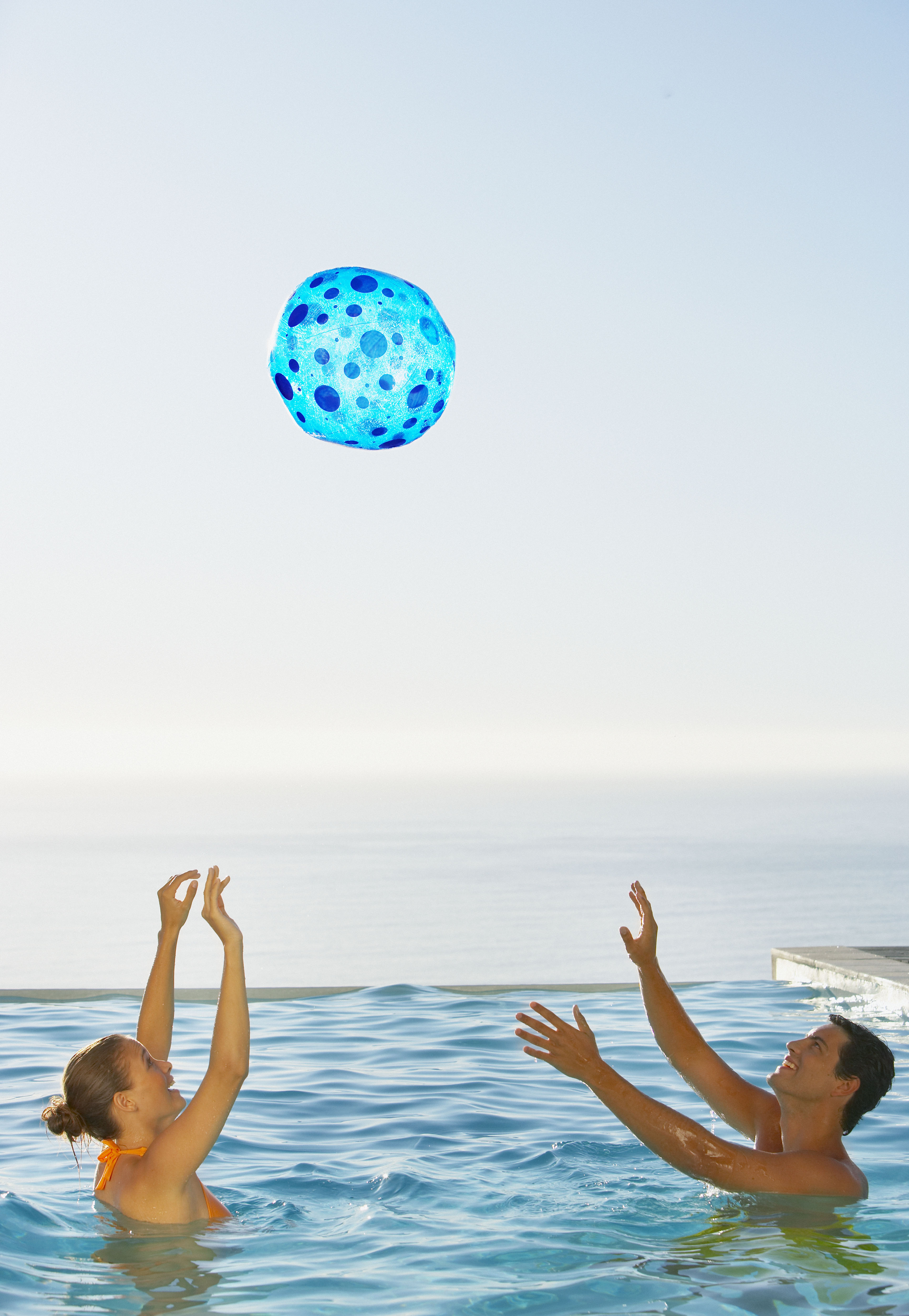 Pareja juguetona disfrutando de un juego con una pelota de playa vibrante junto a la piscina.
