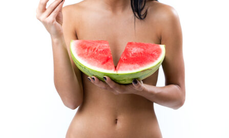 Glad kvinne i grønn bikini nyter vannmelon på en solfylt sommerdag.