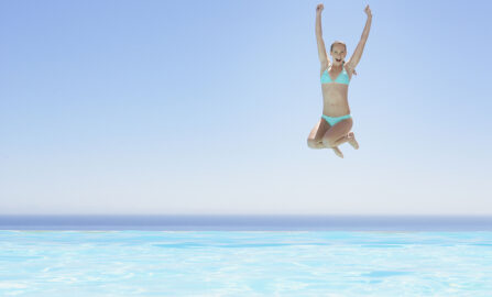 Joyful woman jumping into a stunning infinity pool on a bright summer day.