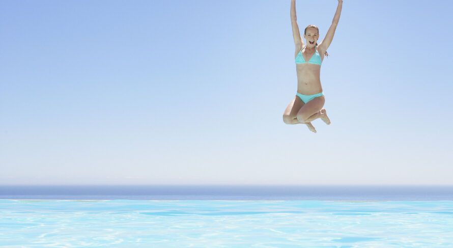 Joyful Summer Jump into Infinity Pool Joyful woman jumping into a stunning infinity pool on a bright summer day.